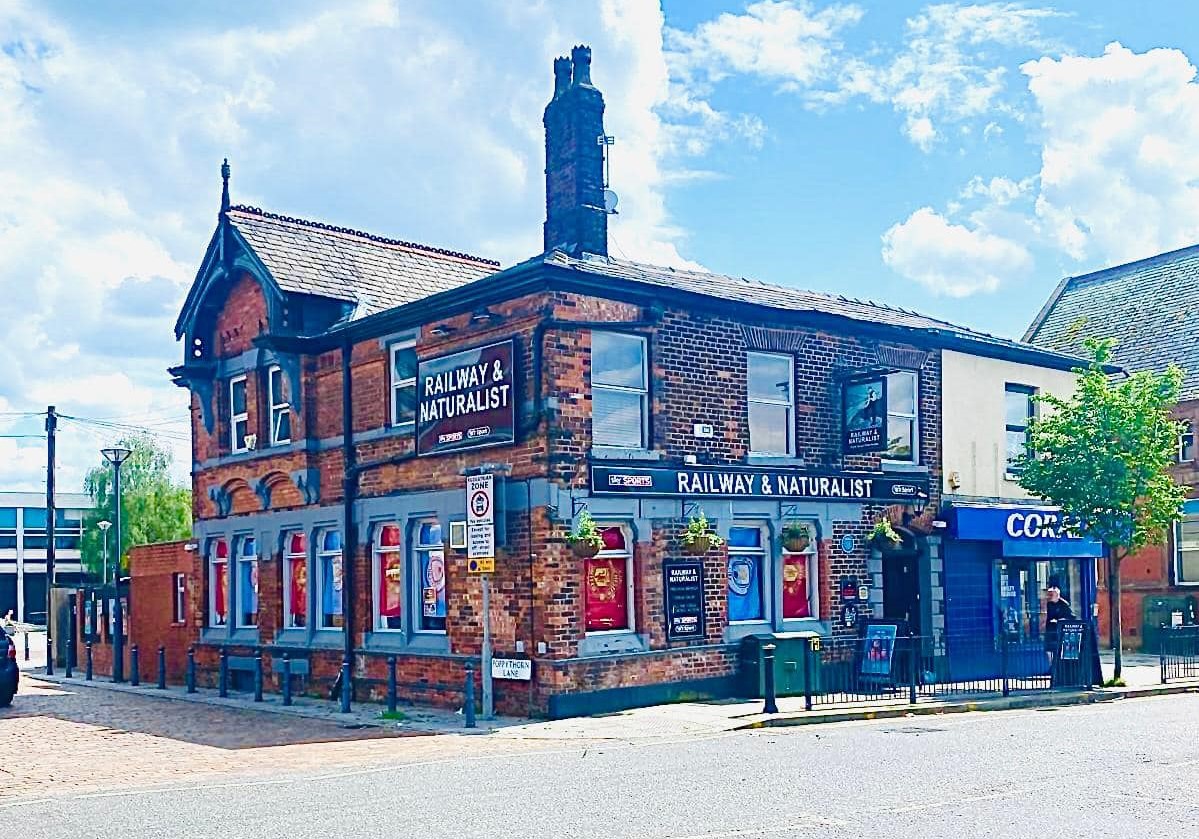 outside railway and naturalist pub in prestwich with man united and city flags in windows, one of the craft union pubs in greater manchester giving away free drinks