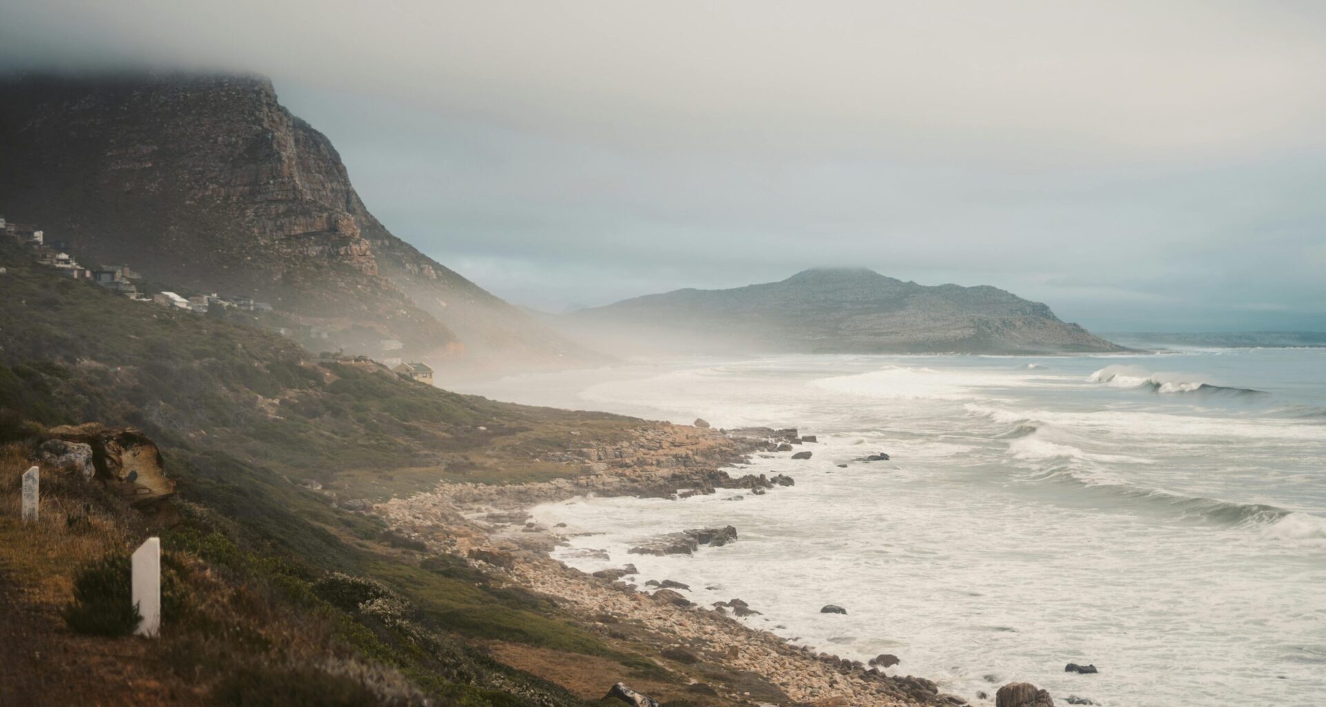 Foggy coastline with waves and hills in background.