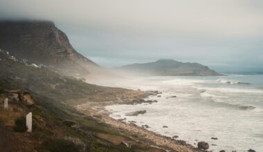 Foggy coastline with waves and hills in background.