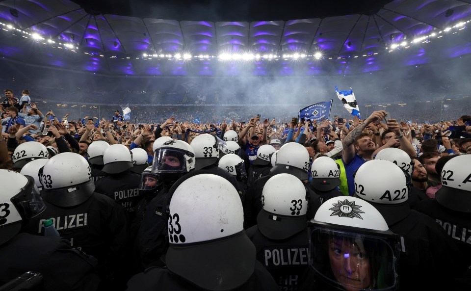 Police officers in riot gear face celebrating soccer fans.