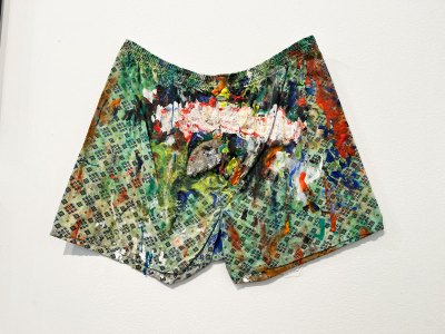 A pair of boxers that has various abstract markings on it. In the center is a stretch of white paint onto which there is writing scrawled. 