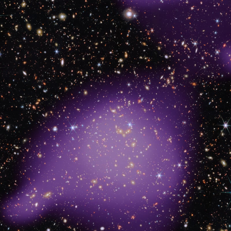 A dense cluster of stars and galaxies fills the image, with a large, faint, purple-hued cloud overlaying the center, depicting dark matter or cosmic gas in deep space.