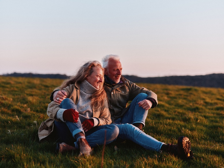 Senior couple sitting in a grassy field at sunset.
