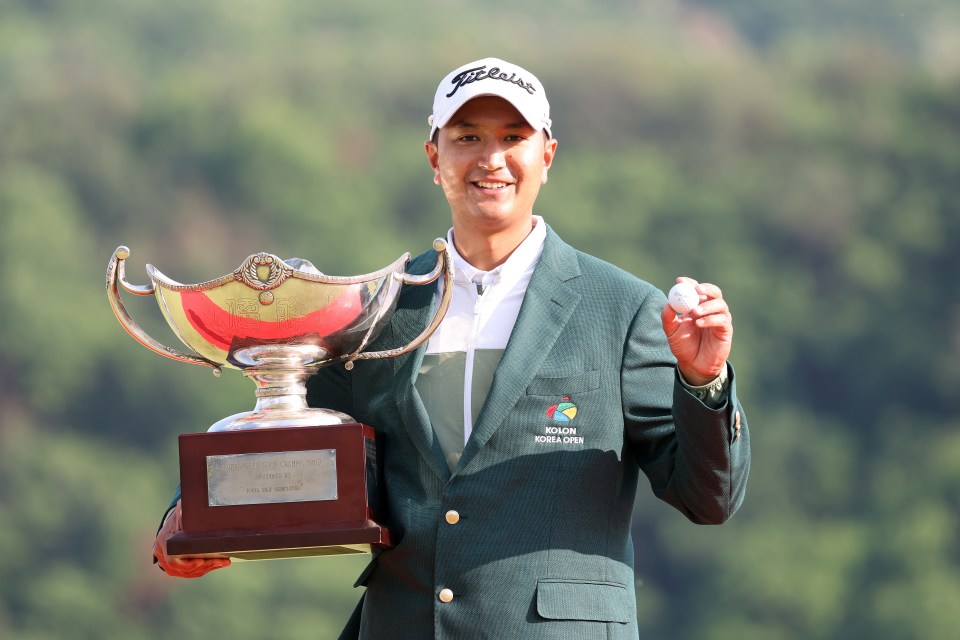 Golfer Sadom Kaewkanjana of Thailand kneeling and holding a championship trophy.