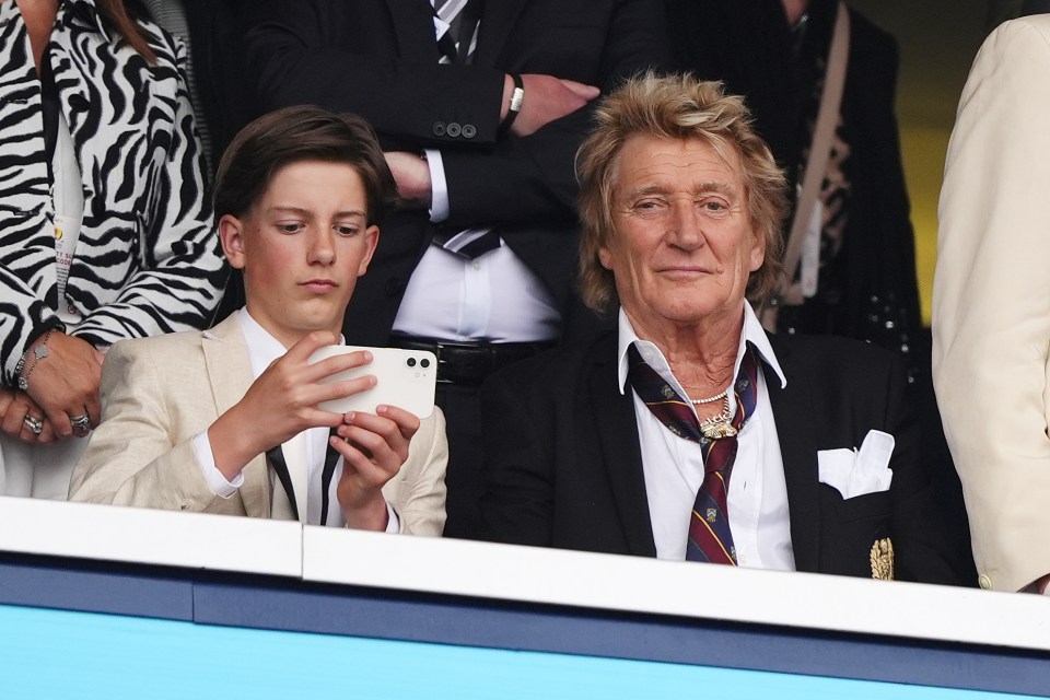 Rod Stewart and a young man taking a photo with a cellphone.