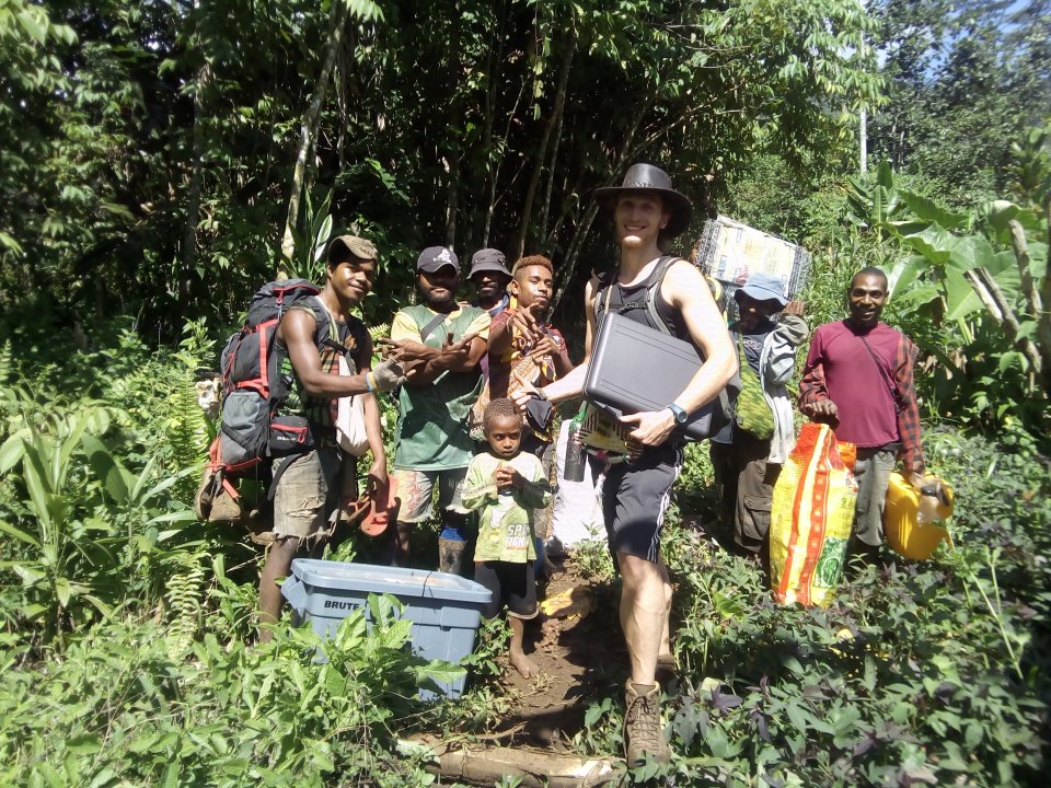 A researcher and local people carrying supplies through a tropical forest.