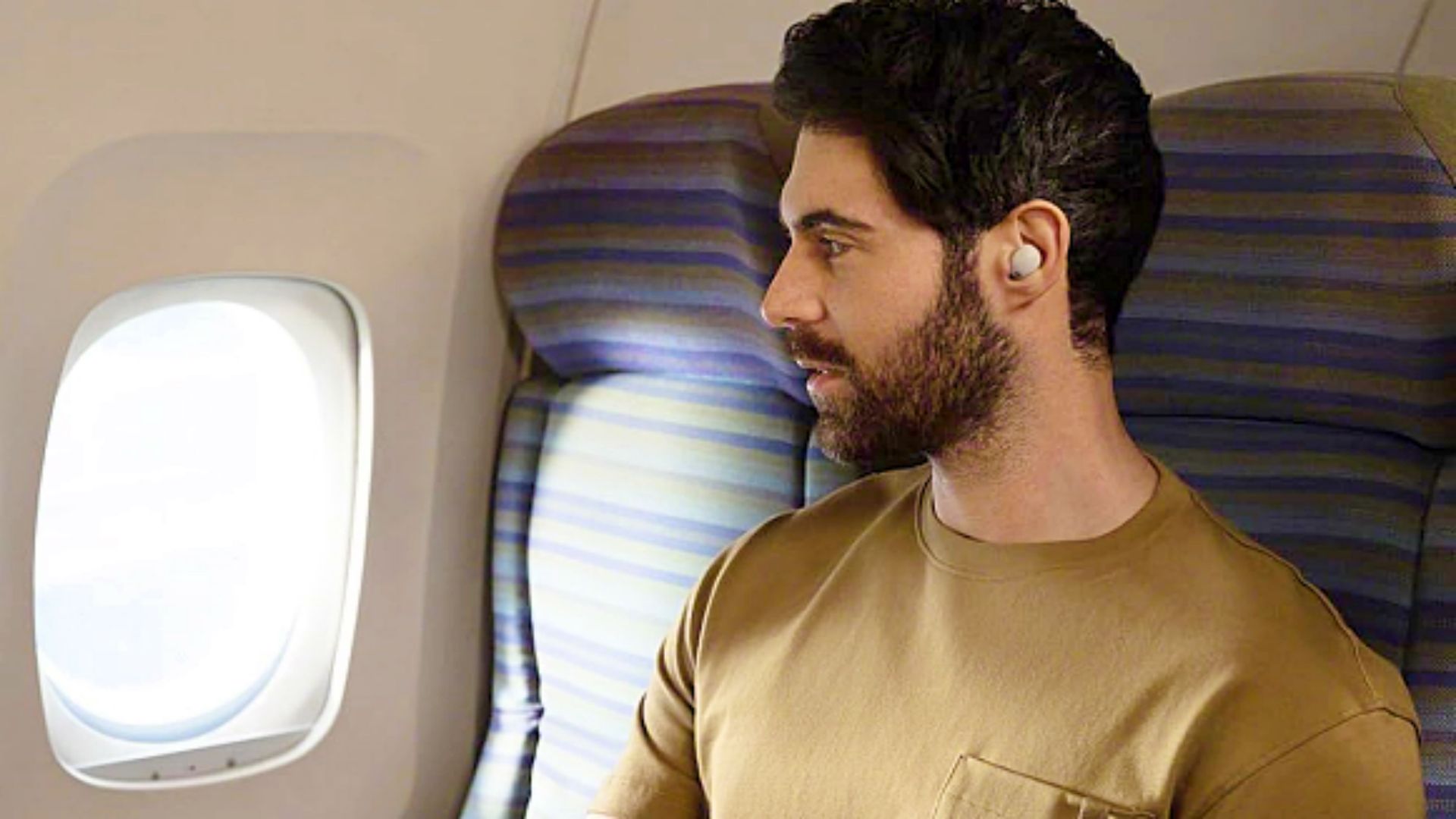 A man looking out an airplane widow while wearing the Sony WF-1000XM5 earbuds,