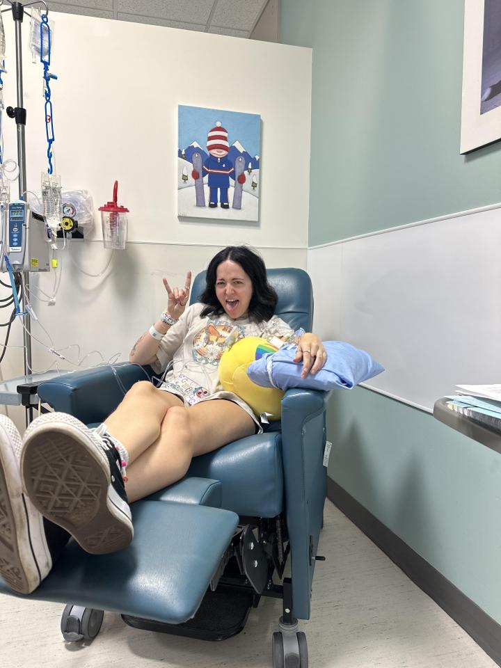 Young woman receiving immunotherapy treatment, giving the rock-on hand gesture.