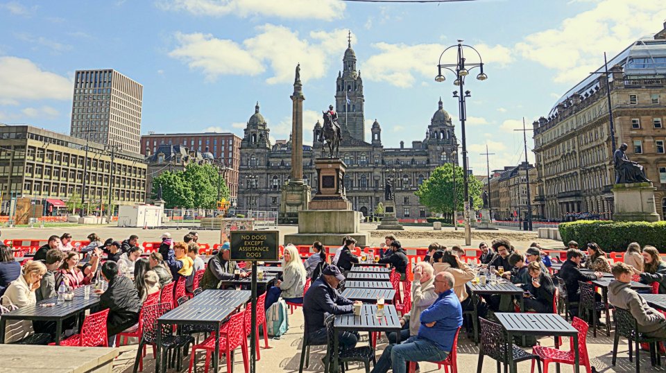 People seated at outdoor tables in Buchanan Street, Glasgow, Scotland, with the Glasgow City Chambers in the background.