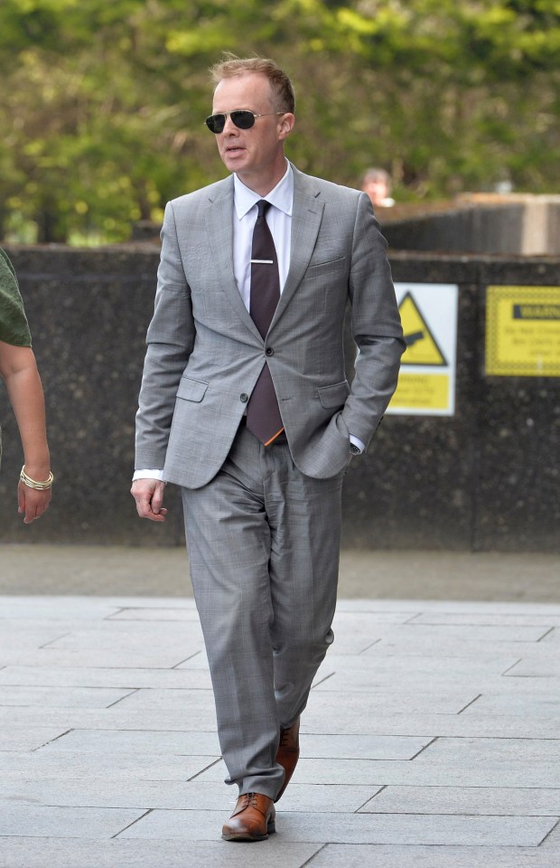 A man in a gray suit and sunglasses walks outside a courthouse.