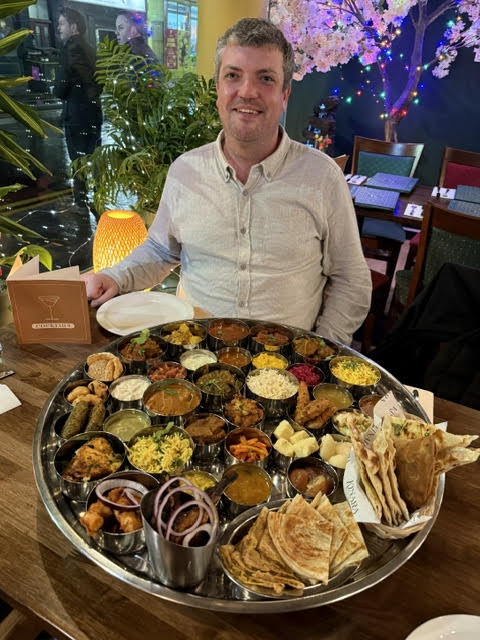 Man sitting at a table with a large platter of Indian food.