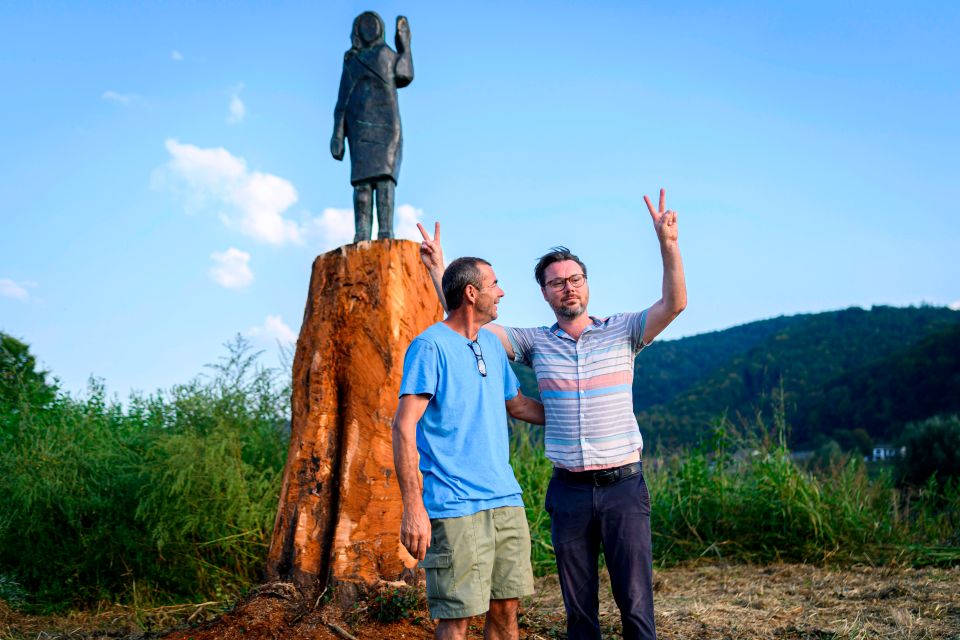 Two men stand near a bronze replica of Melania Trump.