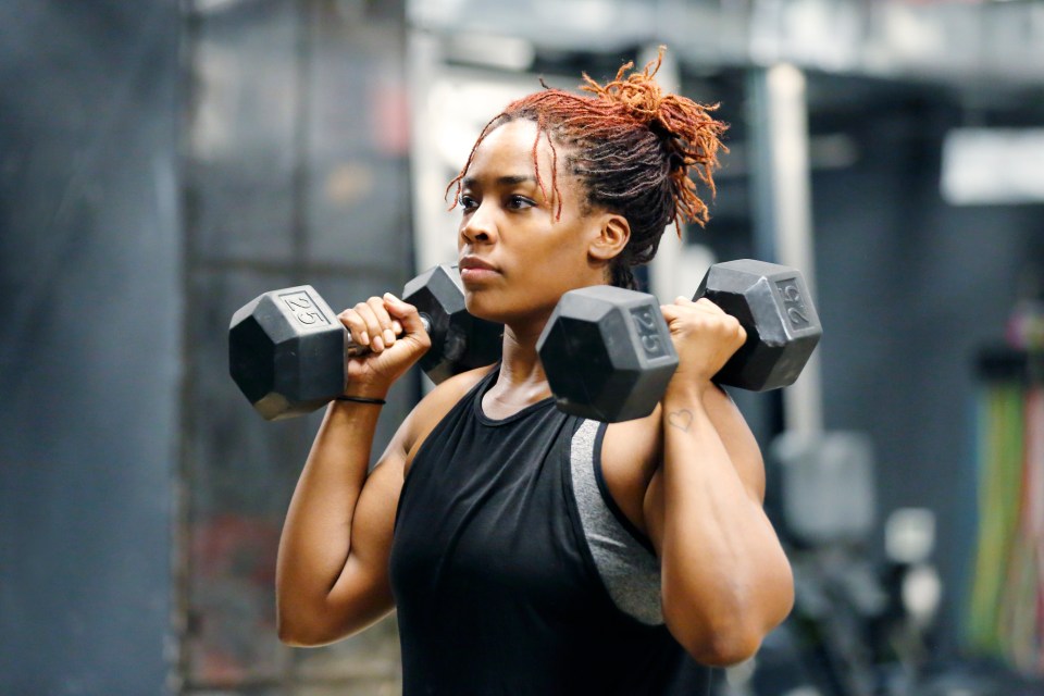 A young African American woman lifting weights at the gym.