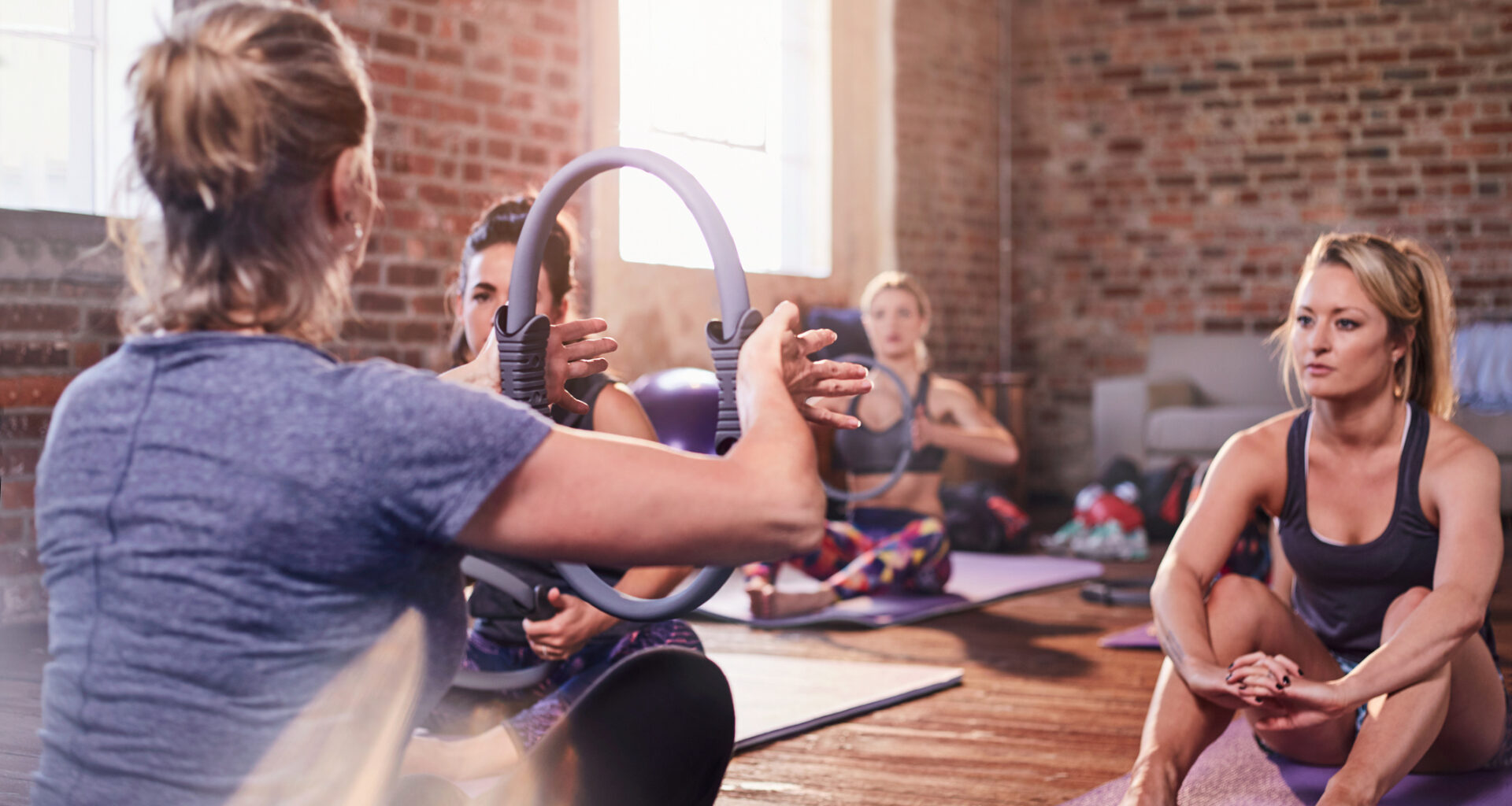 Women in fitness class facing teacher who holds up a Pilates ring