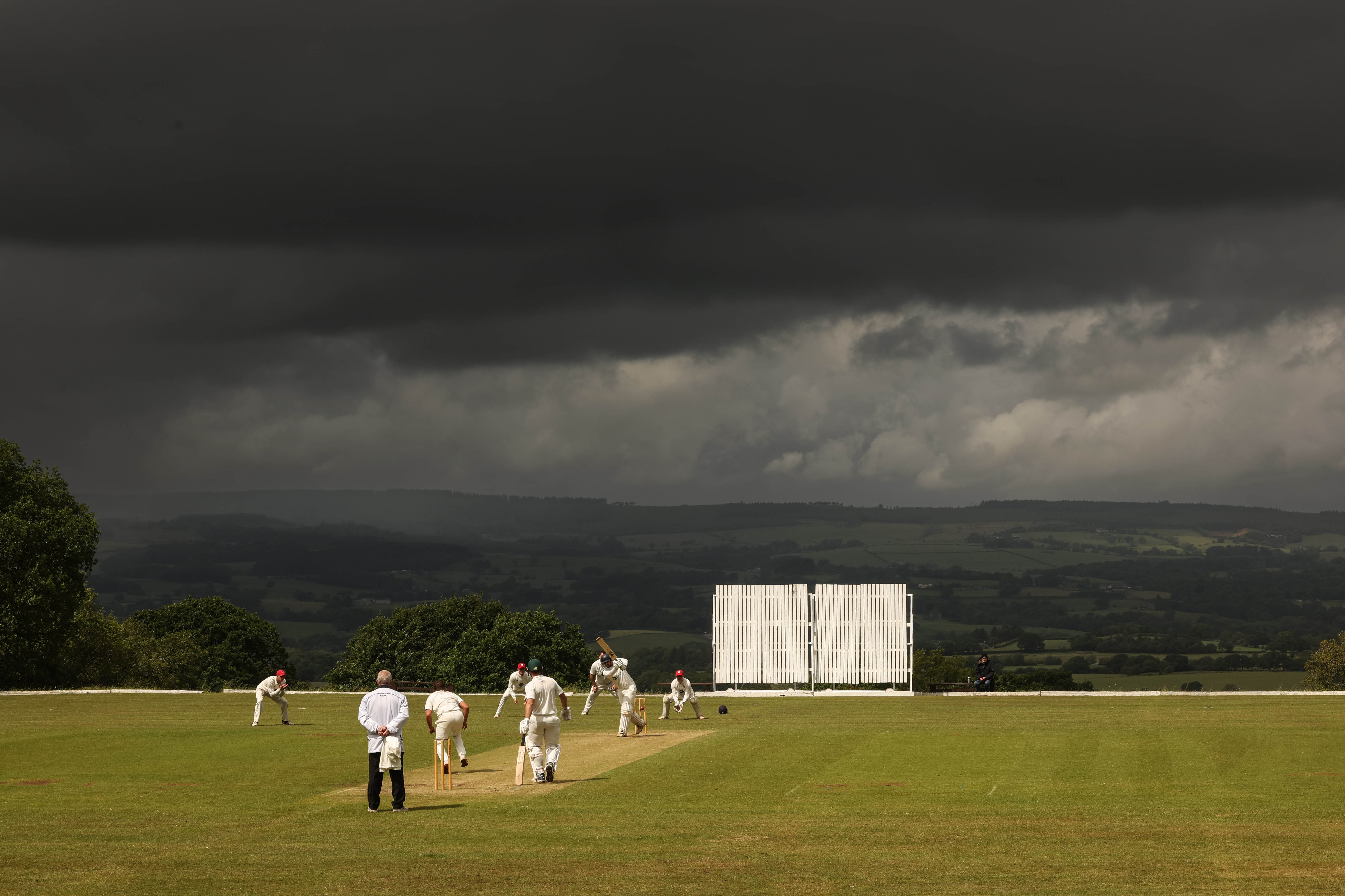 Cricket match in progress under a dramatic sky.