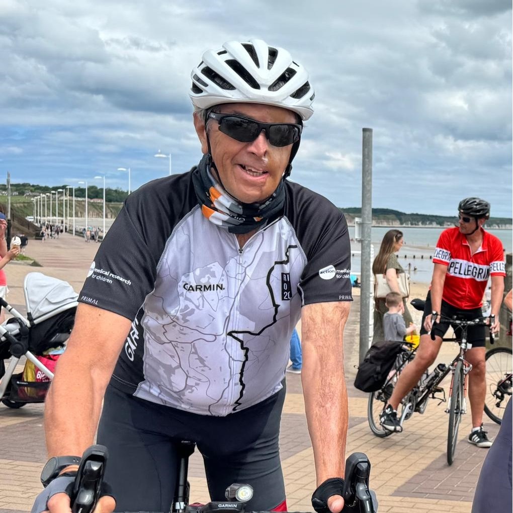 A cyclist in a cycling jersey smiles at the camera.