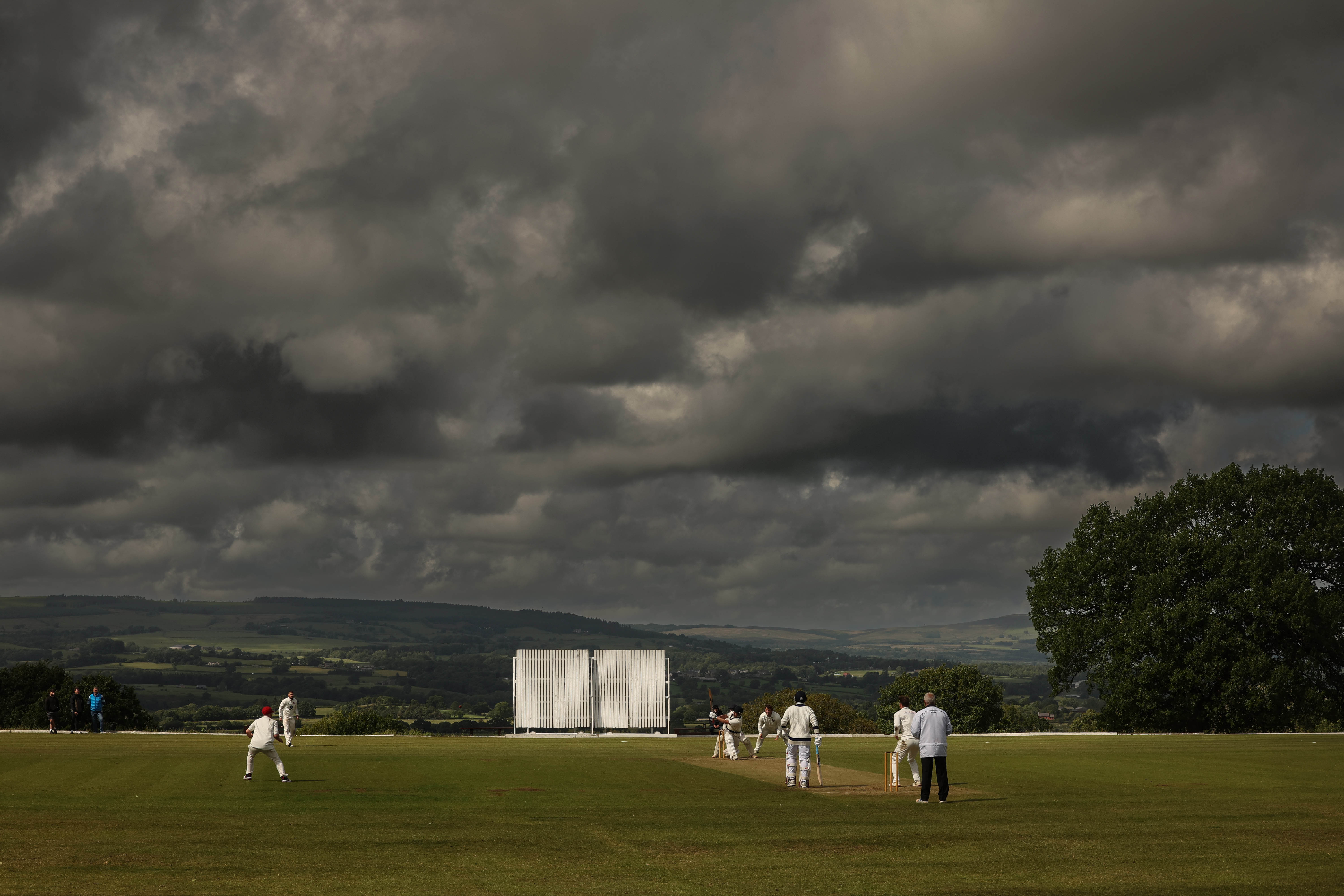 Cricket match in progress under a dramatic sky.