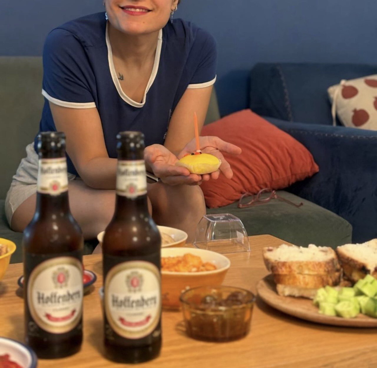 A woman celebrates a birthday with a small cake and beer.