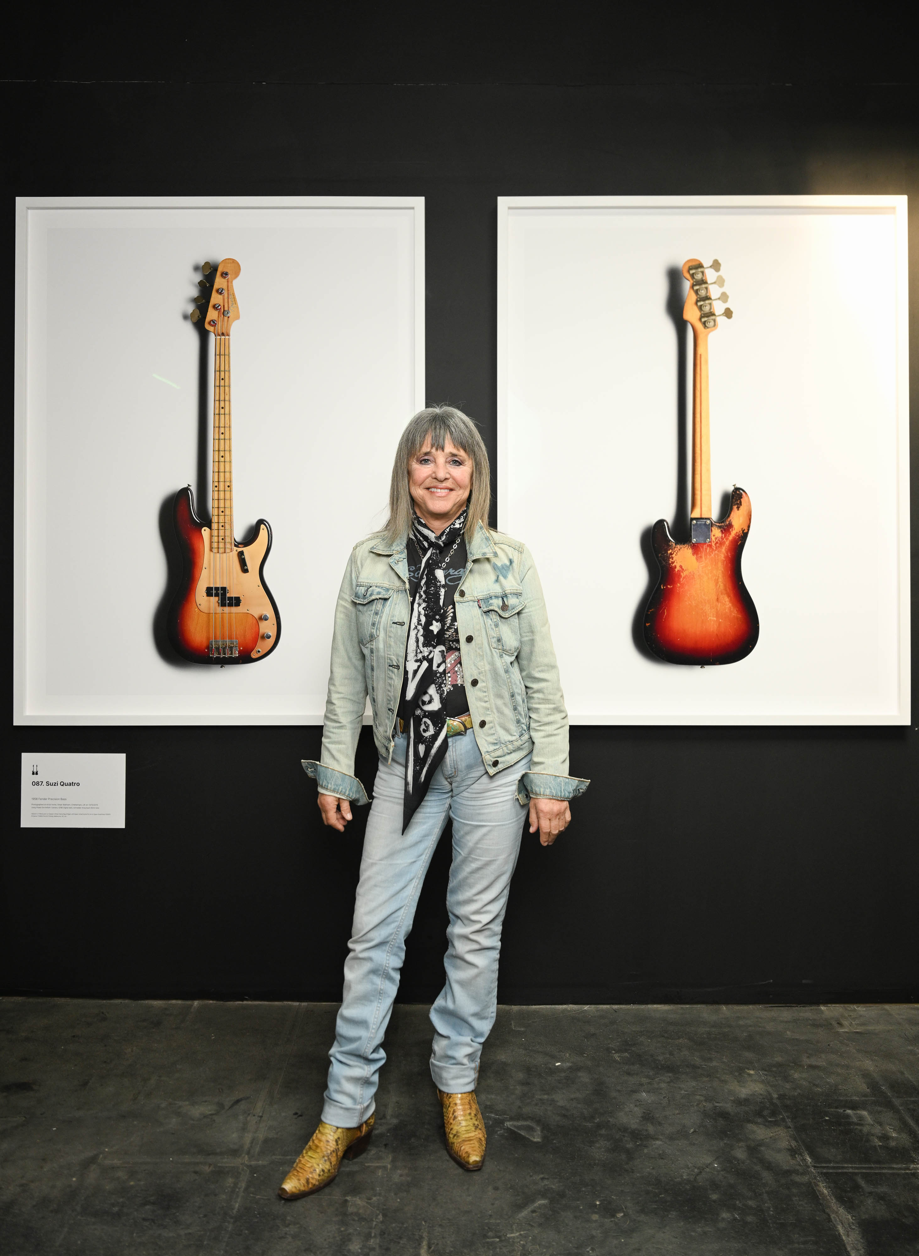 Suzi Quatro standing in front of two framed photos of her basses at the Scale exhibition.