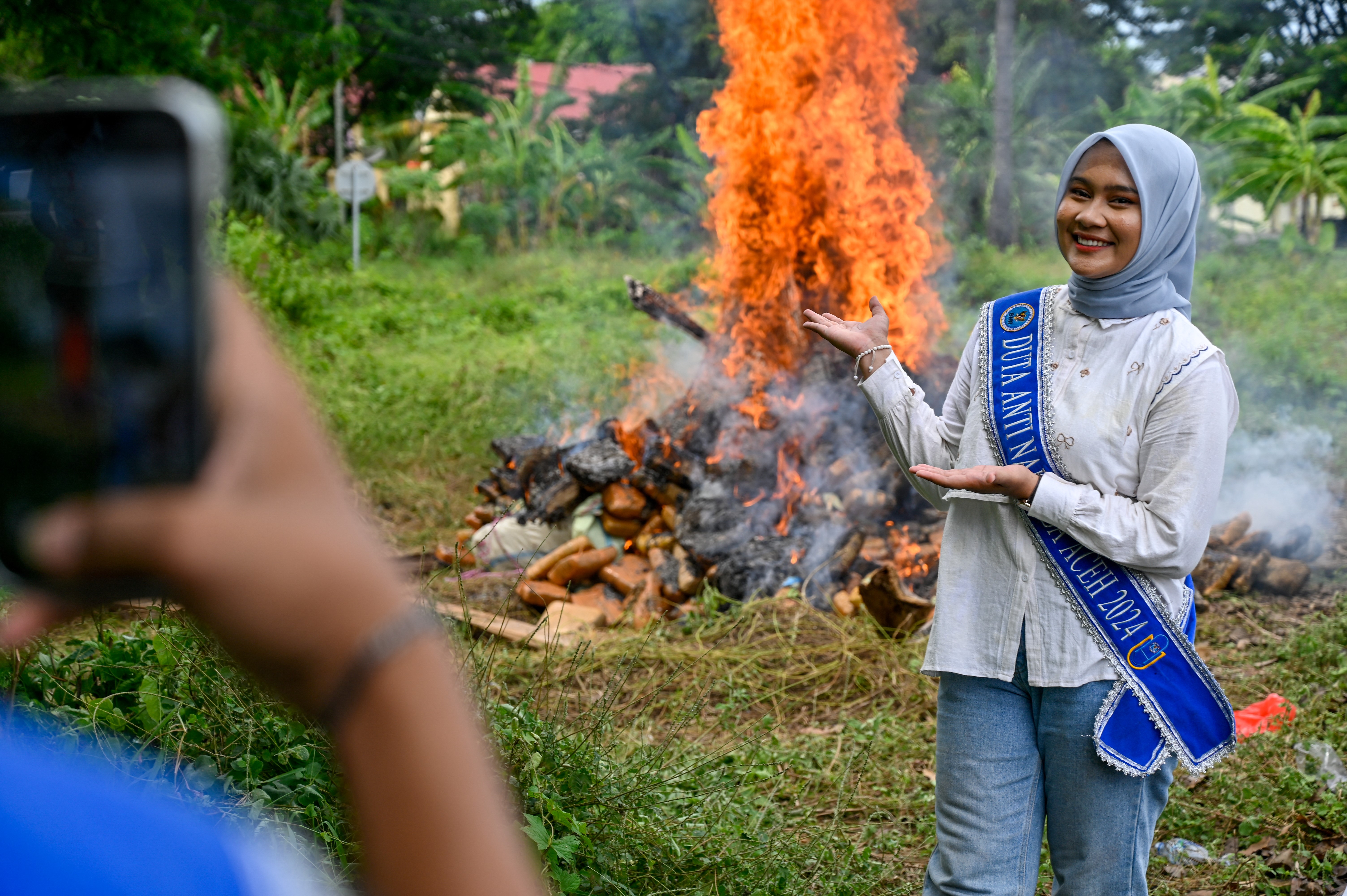 Woman gesturing towards a bonfire burning seized drugs at a press conference.