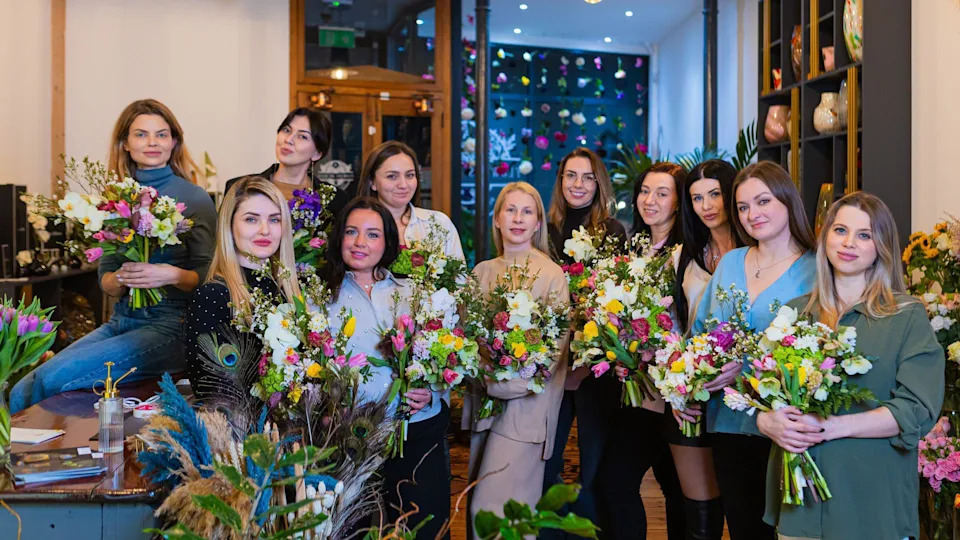 A group of 11 women who took part in a floristry session at a florists in Totterdown in Bristol hold up their floral creations as they pose for the camera
