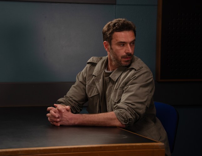 John is sitting in a police interview room looking worried in Emmerdale