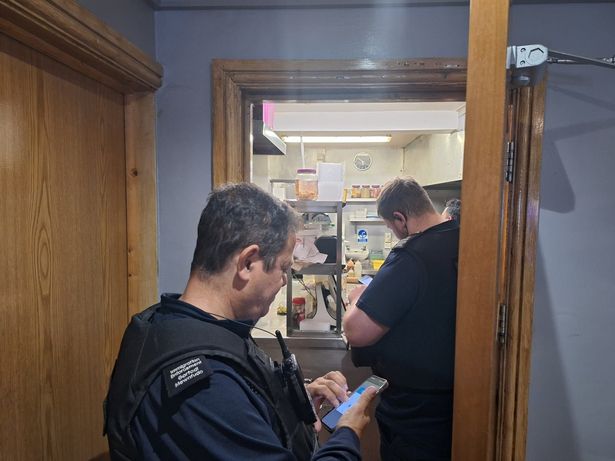 A shot of an open door leading to a kitchen where a few officers are quizzing staff who are not pictured