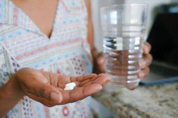 A close-up image of a woman in a kitchen taking medication