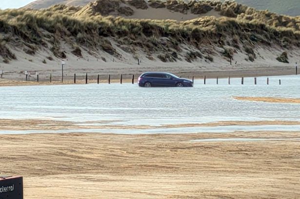 A car caught out by the rising tide at Traeth Ynyslas beach sinking into the water