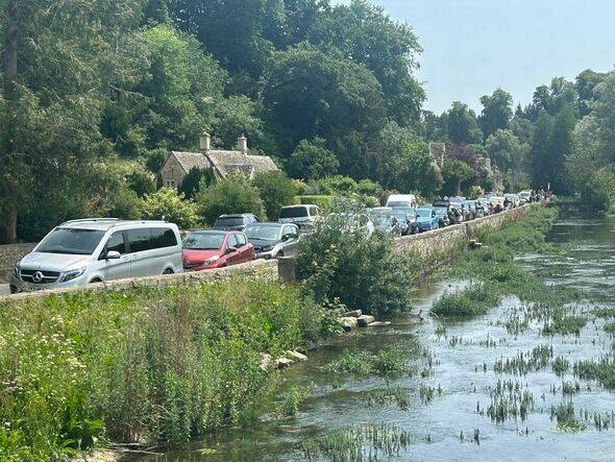 Cars parked along the side of the road beside the river in Bibury 