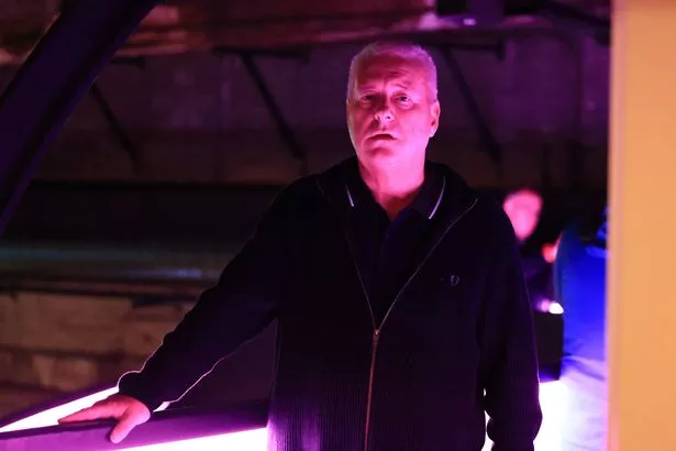 A man dressed in a dark polo shirt and hoodie walking through a warehouse building