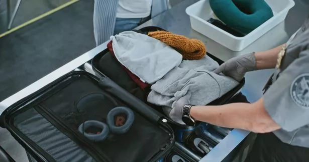 Security Checkpoint in International Airport Terminal: Security Officer Examining Suitcase of Passenger on Conveyor Belt for X-ray Scanning. TSA Baggage Screening Procedures. High Angle Close Up.