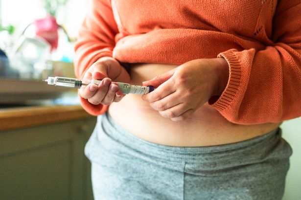 Close up of a woman's hands holding a weight loss injection pen. She is preparing to inject the dose into her abdomen.