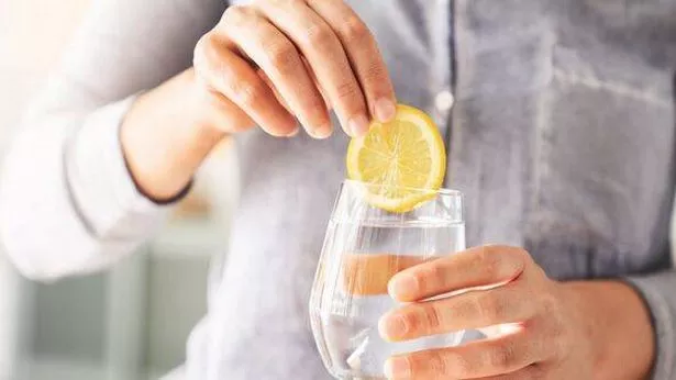 Glass of water with lemon slice in hand of woman