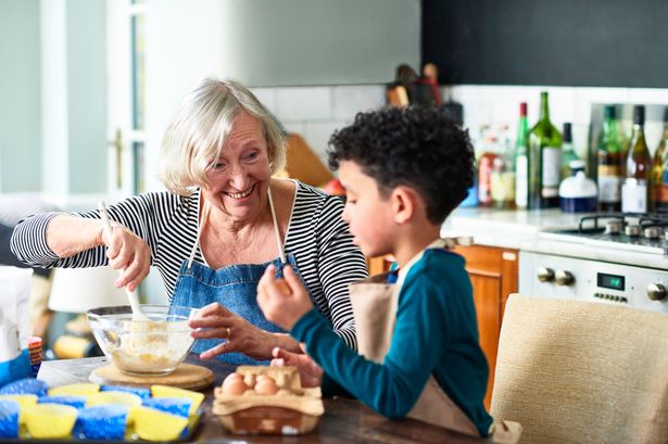Grandmother making cupcakes with young boy at table in kitchen, learning, togetherness, domestic life