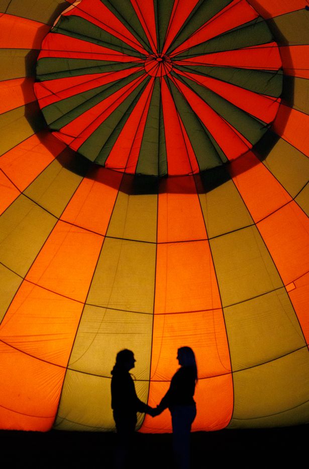 Hot air balloons light up the night sky tonight, Saturday 10 August 2024, at the traditional night glow at the  Bristol International  Balloon Fiesta at Ashton Court.    A couple share a kiss silhouetted by a lit up hot air balloon.   PHOTO:PAUL GILLIS / Reach Plc