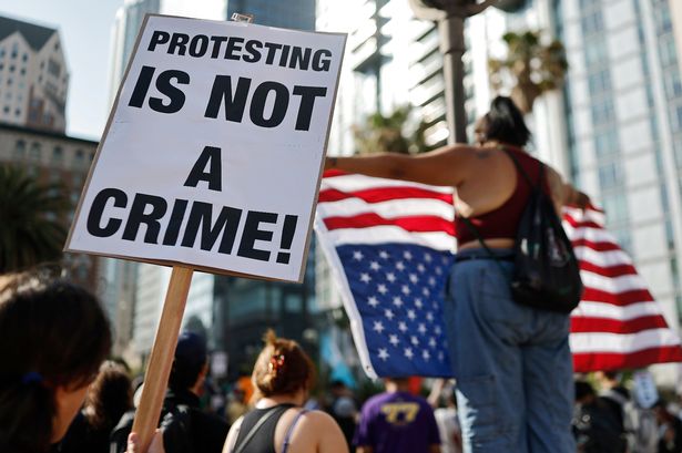  A person holds a "Protesting Is Not A Crime!" sign as people demonstrate before marching downtown as protests against ICE immigration raids continue in the city on June 11, 2025 in Los Angeles, California.