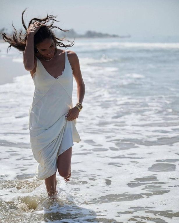 Meghan pictured frolicking in the sea smiling in a white dress