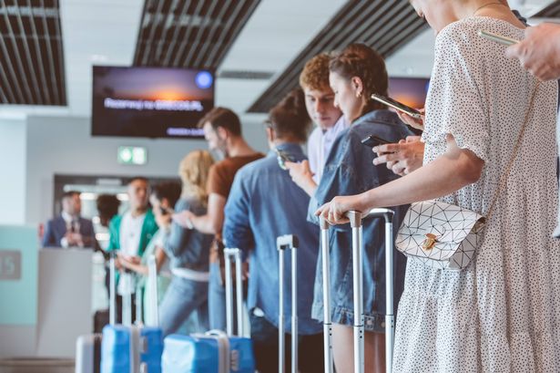 Travelers with luggage using smart phones while waiting in line for boarding at airport.