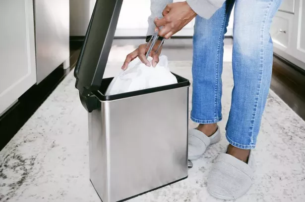 A girl closing the bin bag about to lift it out of her kitchen bin 