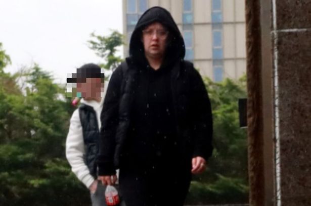 An image of a woman wearing a black coat with the hood up and black trousers, walking towards the camera