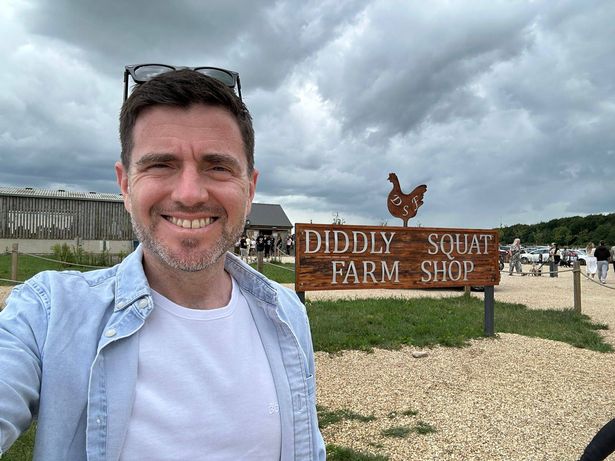 Steffan Rhys takes a selfie next to a large sign for Diddly Squat Farm Shop