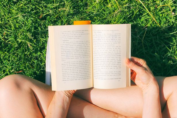 Lovely young woman sitting on the grass in park and reading the book, enjoying life with no technology involved.