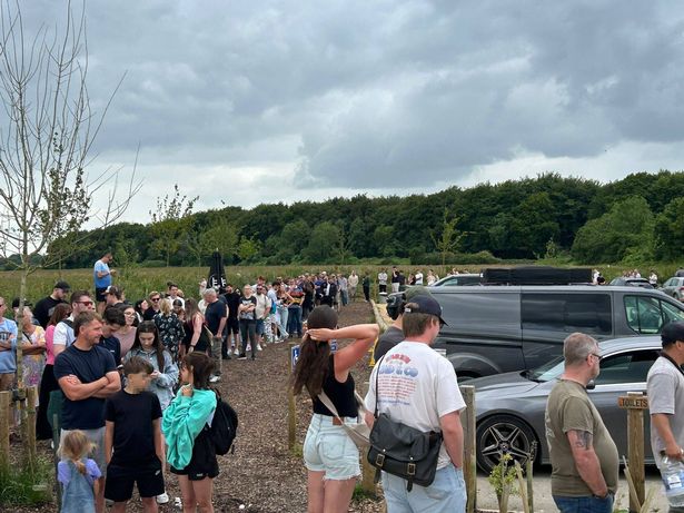 The long queue for the farm shop snakes around parked cars with dozens of people visible queuing