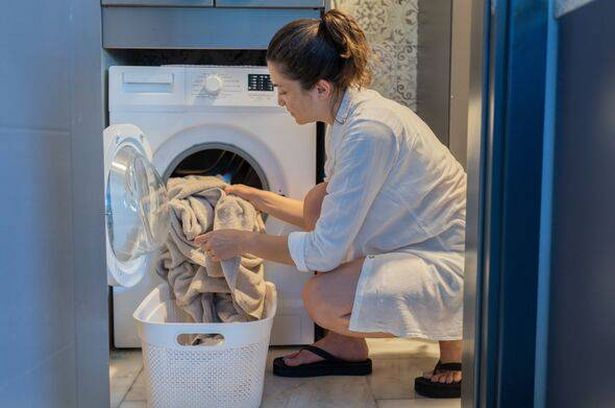 Woman Loading Clothes Into Washing Machine In Laundry Room