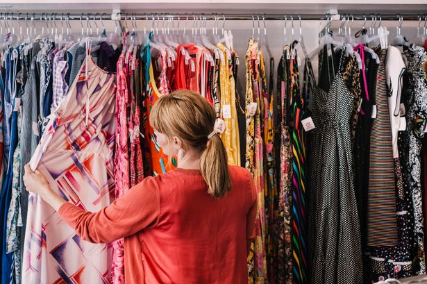 Woman looking at dress hanging on rack in clothes store (stock photo)