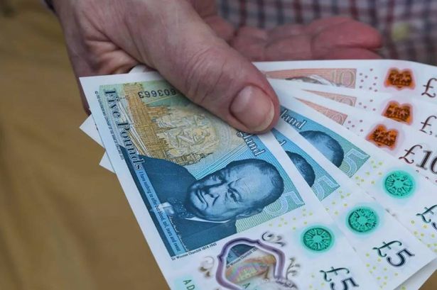 A person's hand holding a set of new UK bank notes fanned out
