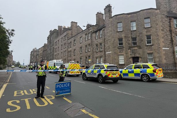 An image of a street with flats along one side, taped off by police with around eight emergency vehicles parked along it.