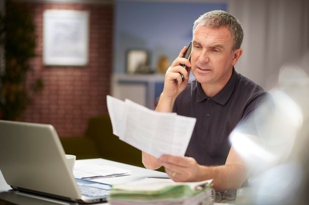 A mature man sits at his dining table at home looking through some bills and paperwork