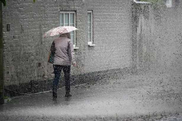 A pedestrian negotiates a partially flooded footpath as heavy rain begins 